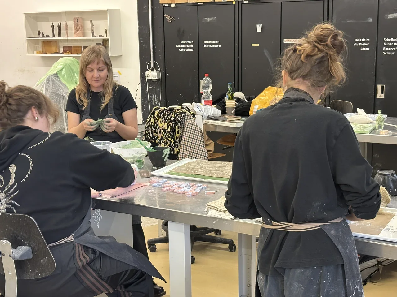 Teilnehmende erkunden Materialien gemeinsam am Arbeitstisch im Atelier
